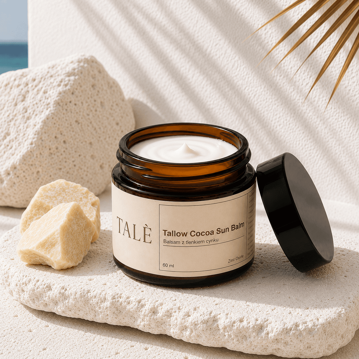 Otwarty słoik balsamu Tallow Cocoa Sun Balm na kamieniu obok masła shea