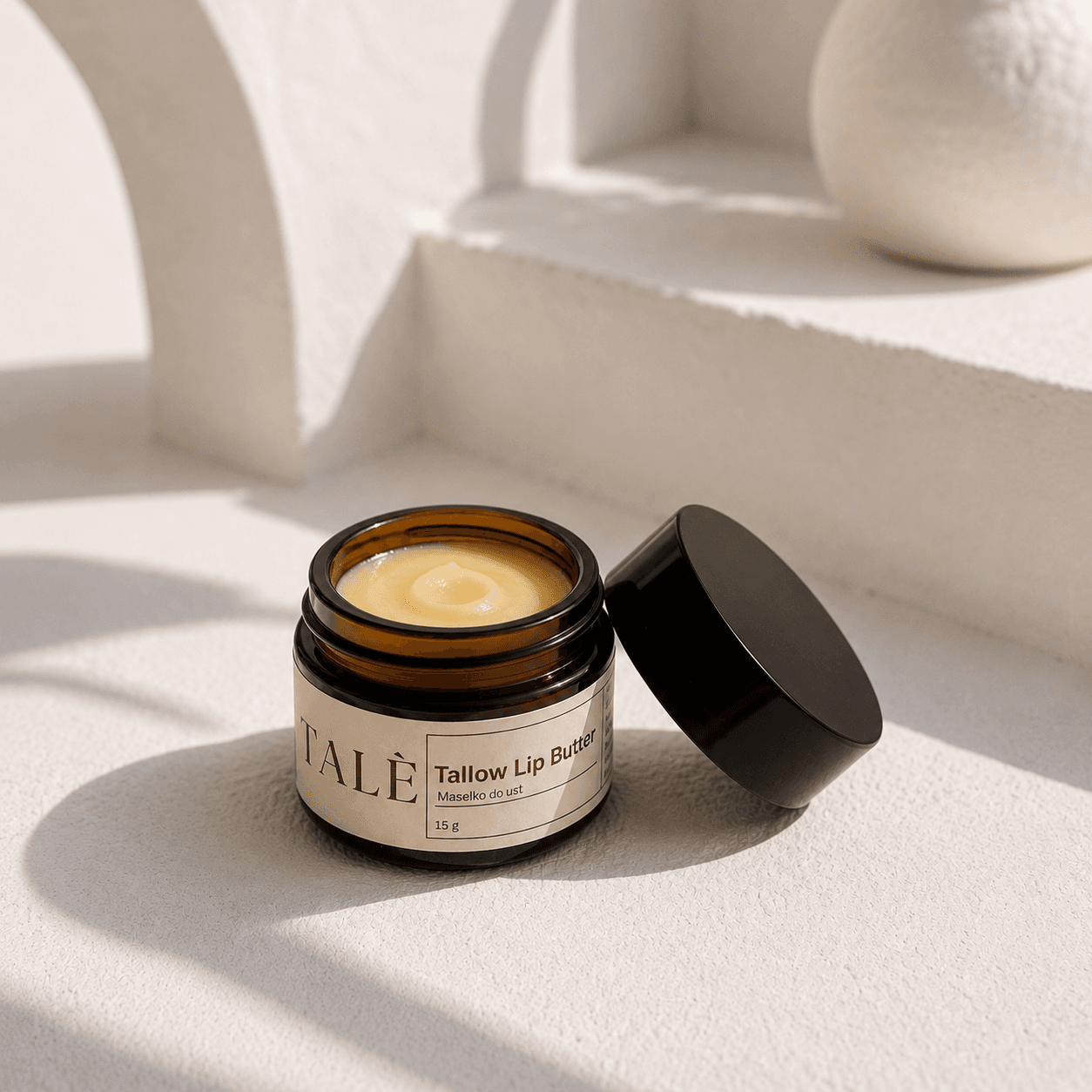 Otwarty słoik masełka Tallow Lip Butter na jasnym parapecie