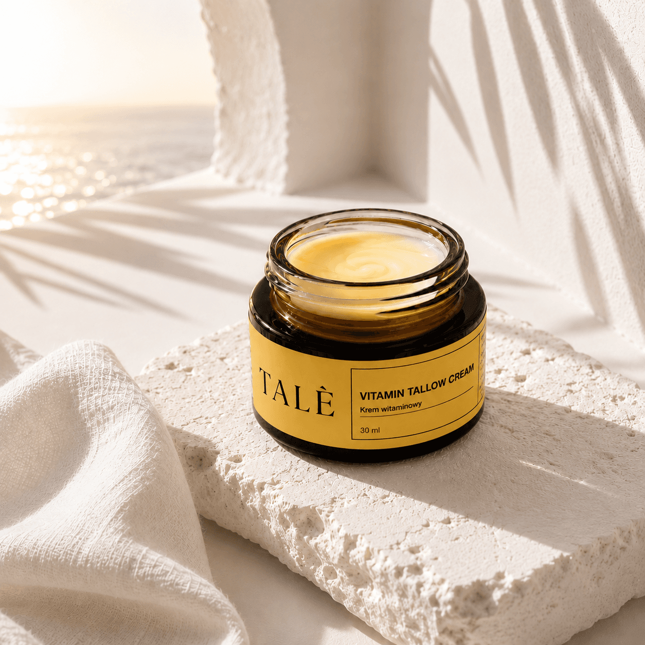 Otwarty słoik kremu TALÈ Vitamin Tallow Cream na kamiennym bloku, w tle morze w słońcu