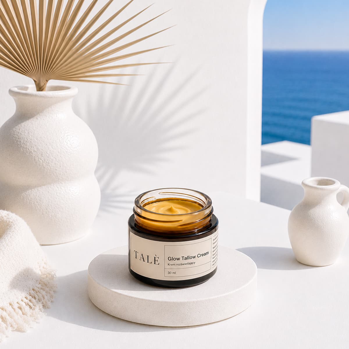 Słoik kremu Glow Tallow Cream na podeście wśród jasnych wazonów, w tle morze