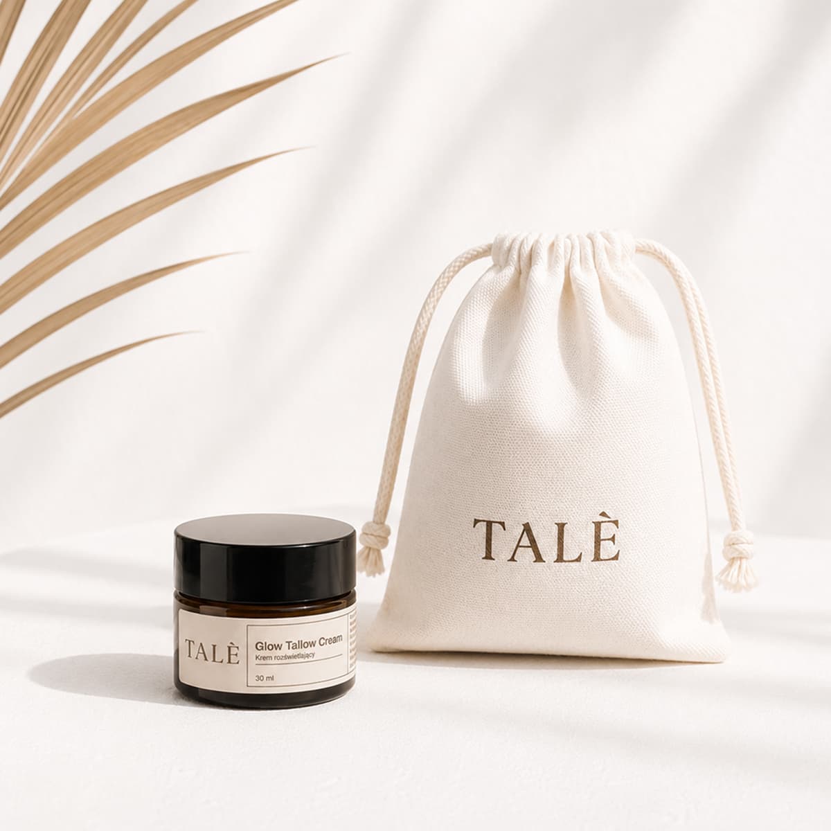 Słoik kremu Glow Tallow Cream obok lnianego woreczka TALÈ w cieniu liścia palmy