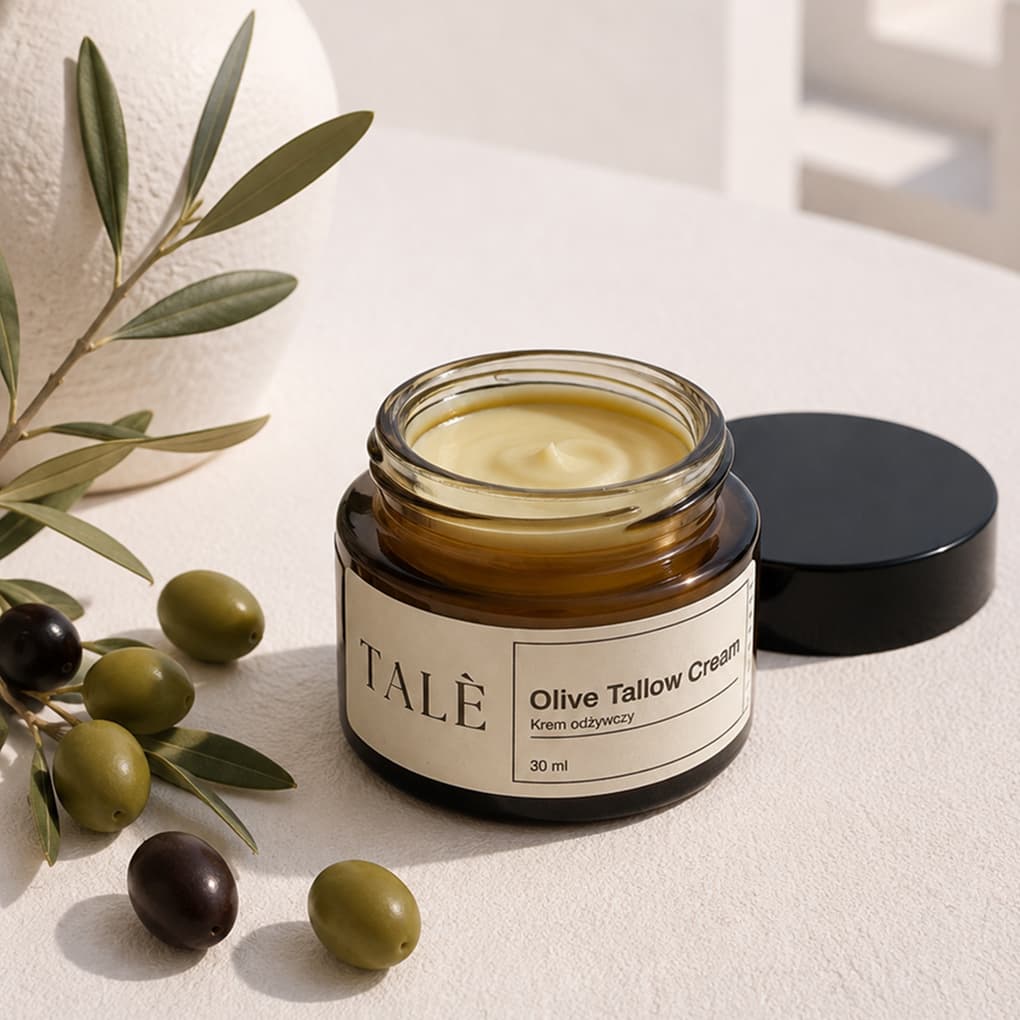 Otwarty słoik kremu Olive Tallow Cream obok oliwek i gałązki oliwnej