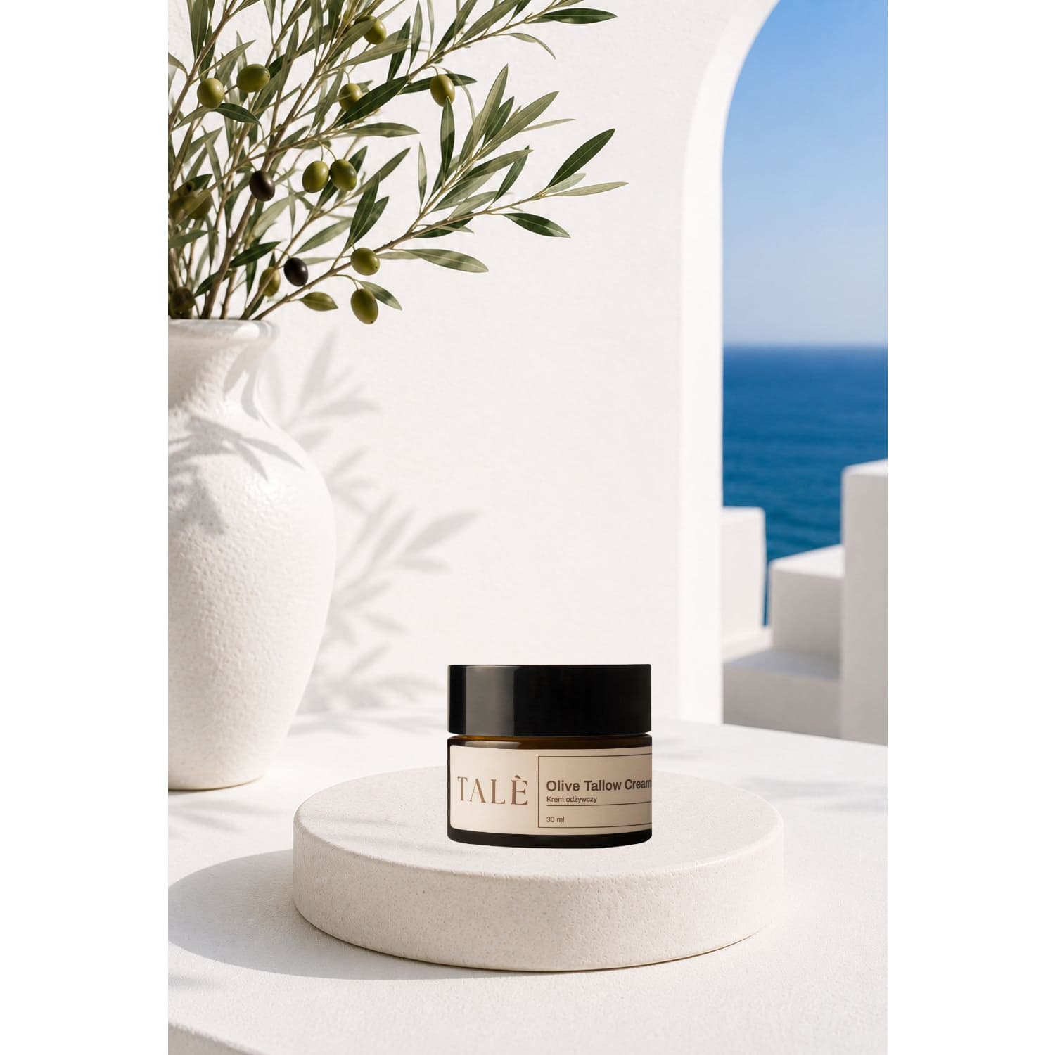 Słoik kremu Olive Tallow Cream na podeście obok gałązki oliwnej, w tle morze