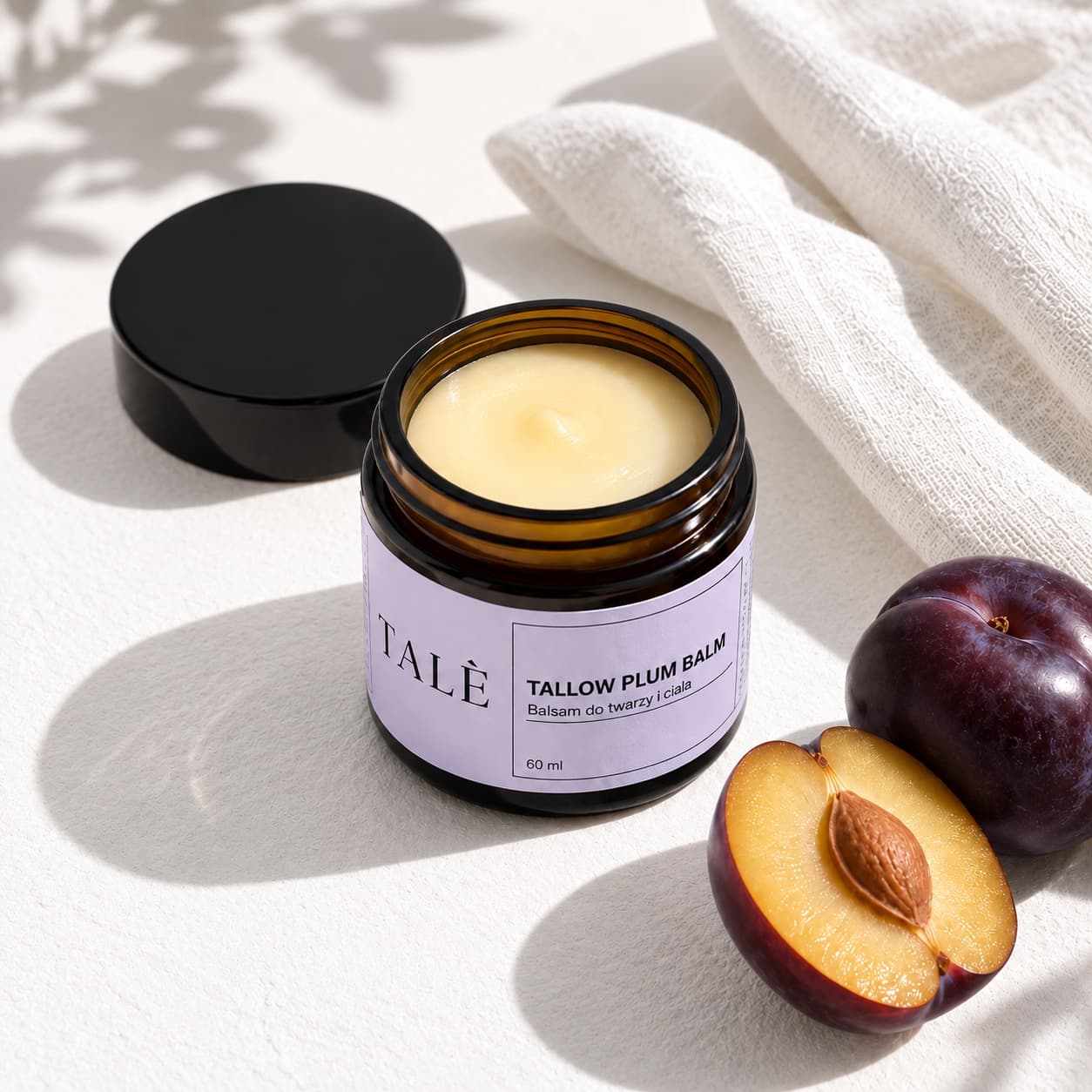 Otwarty słoiczek balsamu TALÈ Tallow Plum Balm obok przekrojonej śliwki