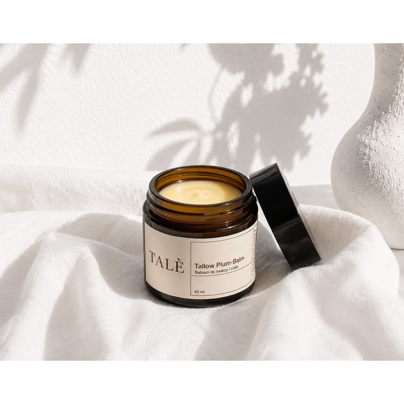 Otwarty słoik balsamu Tallow Plum Balm z kremową konsystencją na białej tkaninie