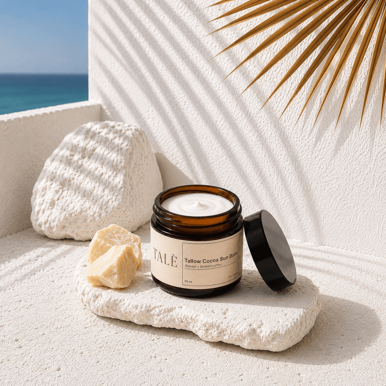 Otwarty słoik balsamu Tallow Cocoa Sun Balm na kamieniu obok masła kakaowego
